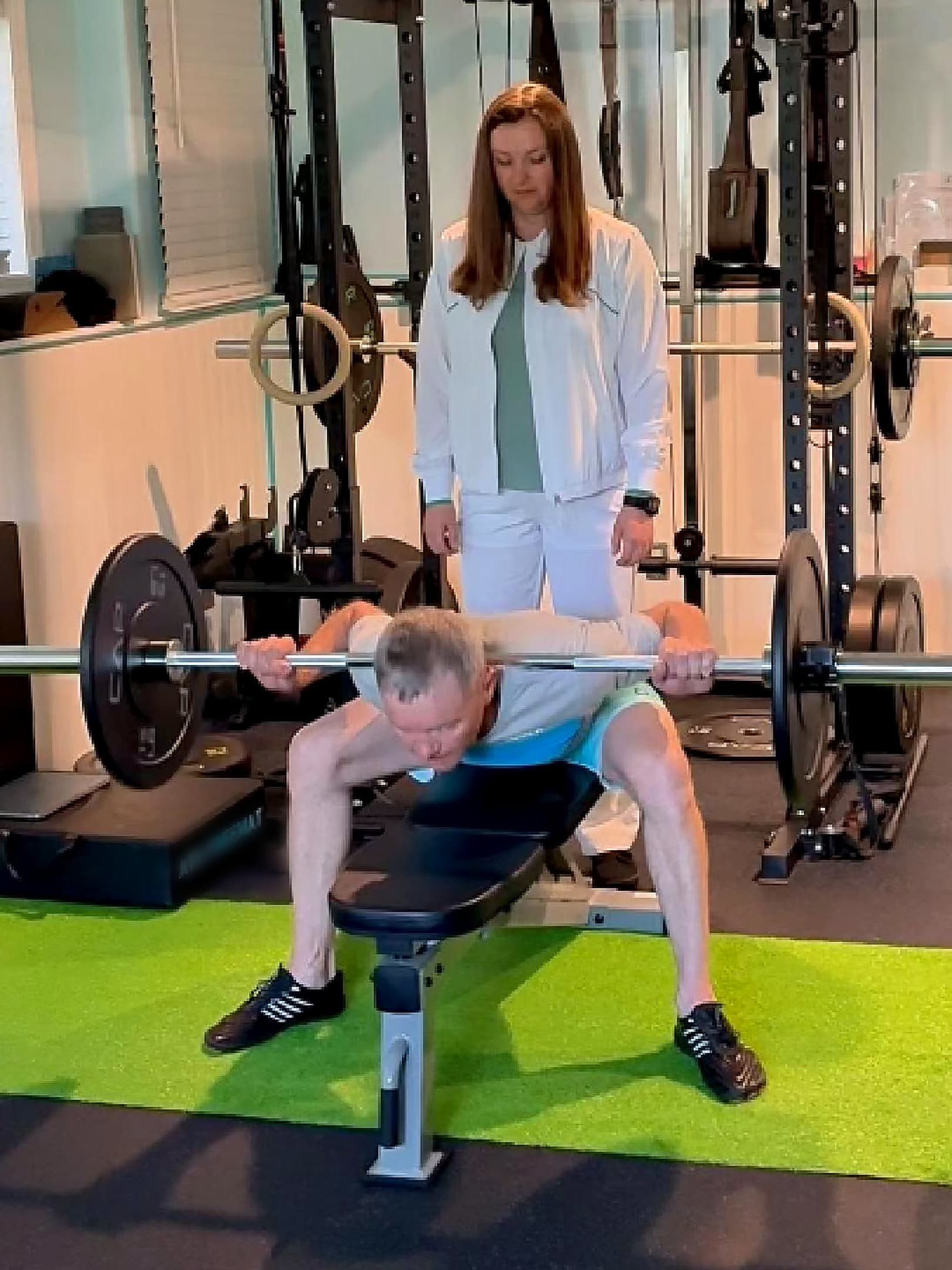 The same client performing a barbell seated good morning with Diana coaching alongside